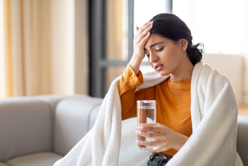 woman with headache and glass of water in hand